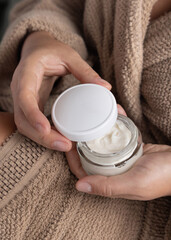 Closeup of woman in brown bathrobe opening white cream jar with hands, cosmetic mockup