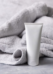 White blank squeeze cream tube near light grey bath towel top view, cosmetic mockup