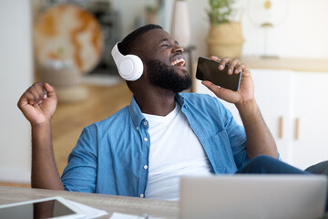 Break In Work. Cheerful African Guy In Blue Shirt Singing At Workplace, Using Phone As Microphone...