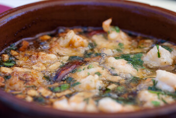 A close-up shows a clay pot brimming with bubbling fried seafood, herbs, and garlic. The golden-brown seafood contrasts beautifully with the vibrant green herbs