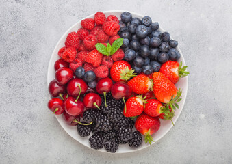 Fresh organic summer berries mix in white plate on light kitchen table background. Raspberries,...