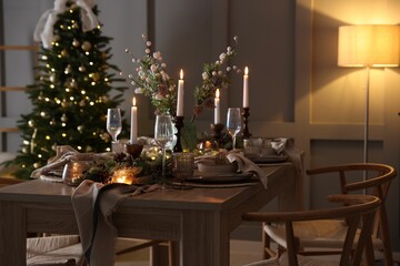 Christmas table setting with stylish dishware, glasses and burning candles in festive decorated room