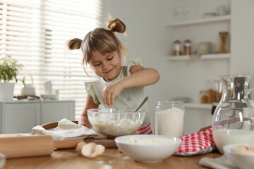 Little helper. Cute girl making dough at table in kitchen