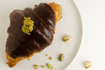 Croissant stuffed with pistachio paste and kadaif dough covered with dark chocolate on a gray plate. Trend food concept. Top view. Copy space. Selective focus.