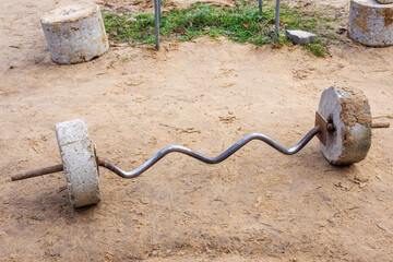 A barbell with concrete pancakes and a curved neck on the sand of the sports field. Sports...