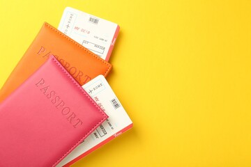 Passports in color covers and flight tickets on yellow background, top view. Space for text