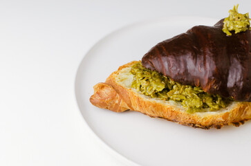 Croissant stuffed with pistachio paste and kadaif dough drizzled with dark chocolate on a white plate. Trendy food concept. Copy space. Selective focus. Banner