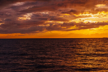the water surface of the sea under a cloudy sky, illuminated by the rays of the setting sun at sunset