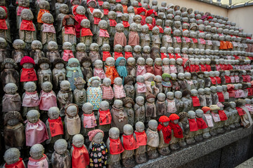 Obraz premium Hundreds of Stone Jizo statues, guardians of children, in Osaka, Japan, wear colorful knitted red hats and red bibs. A tradition offering protection and blessings.