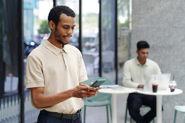 Smiling businessman texting message on mobile phone while working in modern office