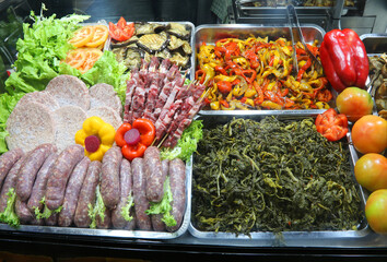 raw dishes with meat, sausages, hamburgers, skewers, and mixed vegetables on trays in the cafeteria