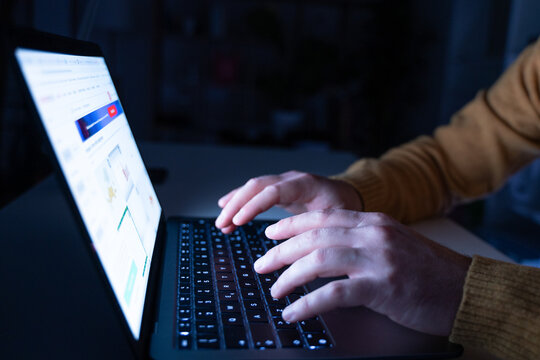 Hands typing on laptop keyboard in the dark