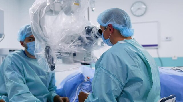 Male surgeon uses metal forceps and turns to look at microscope. Doctors perform neurosurgery using modern technologies.