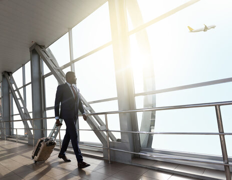 Handsome african businessman walking with suitcase at airport terminal, young african american man going to flight boarding, side view. High quality photo
