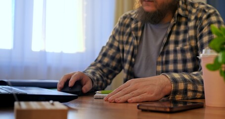 Remote worker wearing glasses, sipping coffee while typing on laptop, sitting at minimalist desk...
