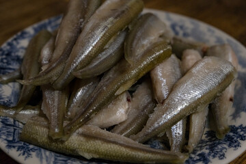 Raw smelt fishes on a plate. Small raw fish, snetok or smelt on a plate.  A portion of raw fresh fish on a plate. Before frying. smelt or horse mackerel. Close-up