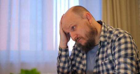 Bald man rubs forehead while stress builds in hectic workspace letting stress overshadow tasks if...