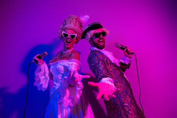 Elegant couple in vibrant masquerade costumes singing under neon lights with purple and violet hues