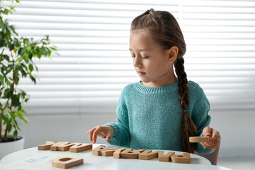 Little girl learning alphabet with wooden letters at white table indoors