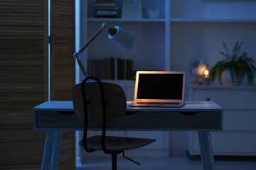 Comfortable workplace with laptop and lamp on table indoors