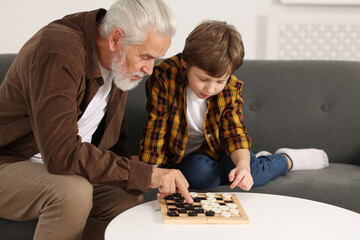 Grandpa and his grandson playing checkers at table indoors