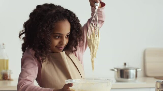 African American girl stirs batter, joyfully engaging in the process of making tasty pastries at home kitchen