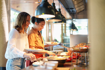 Young adult multiracial and Caucasian females smile while selecting food in a self-service...