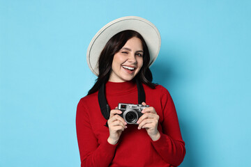 Young tourist in hat with camera on light blue background
