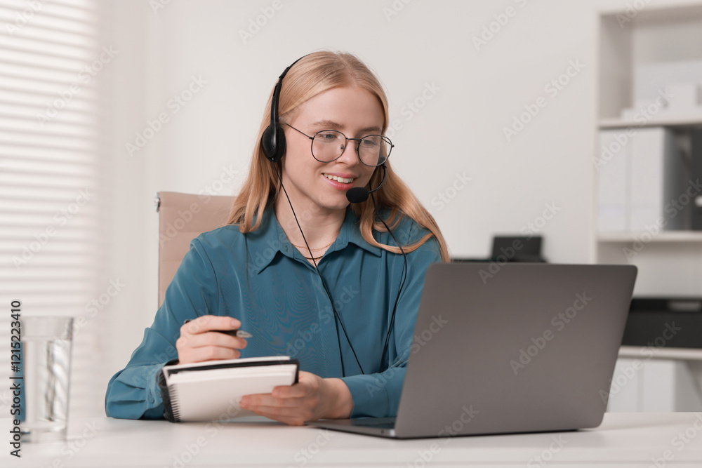 Poster interpreter in headset taking notes while working with laptop at table indoors