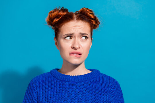 Young woman with red hair wearing blue sweater showing perplexed expression on clear blue background