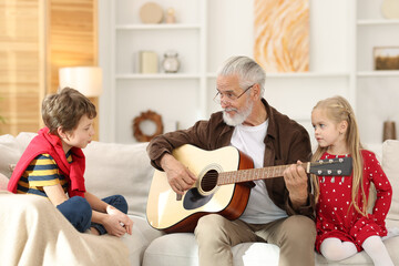 Grandpa playing guitar for his grandkids on sofa at home