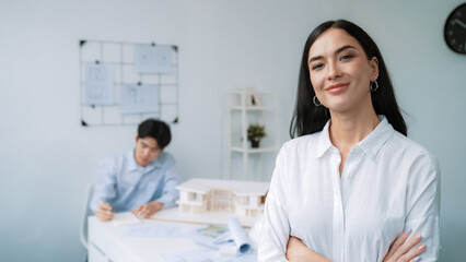 Fototapeta premium Closeup of female professional architect engineer cross arms with confident while skilled coworker focus on drawing blueprint at table with house model. Creative living and design concept. Immaculate.