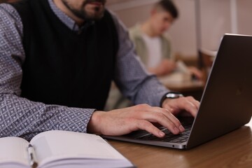 Man typing on laptop near book at desk in library, closeup