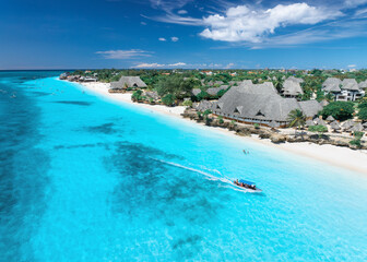 Aerial view of sandy beach, blue sea, bungalows, green palms, umbrellas, floating boat on summer sunny day. Nungwi, Zanzibar island. Travel. Tropical landscape. Top drone view of luxury resort. Ocean