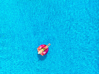 Aerial view of young woman on swimming ring in pool near ocean on summer sunny day. Top drone view...