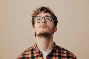 Obraz premium Thoughtful Young Man in Glasses Looking Upward Against a Neutral Background