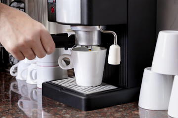 Electric coffee maker filling a white ceramic cup with coffee.