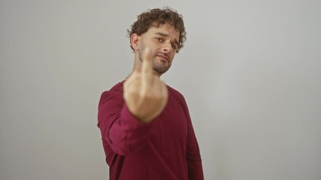 Young hispanic man standing and wearing t-shirt, showing rude 'fuck you' middle finger gesture, expressing impolite attitude over isolated white background