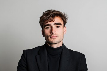 Obraz premium Confident Young Man in Stylish Black Turtleneck and Blazer Against Neutral Background