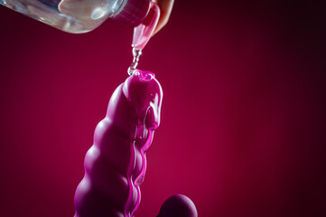 Lube pouring on pink dildo on pink background. 
