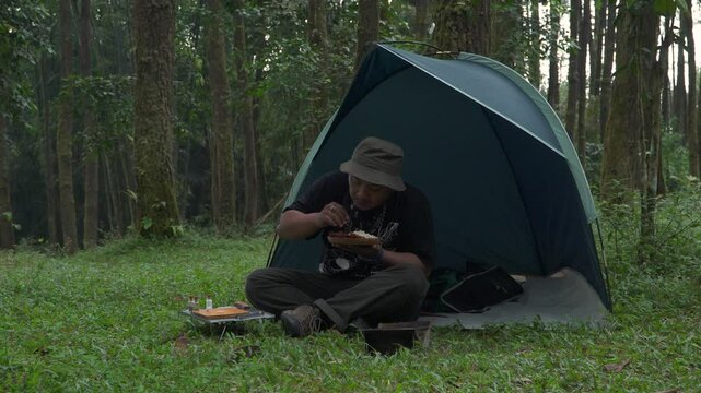 Footage of an Asian male adventurer eating lime leaf rice with grilled shrimp as a side dish that he cooked himself. An adventurer is bushcrafting with simple tools in the lush wilderness