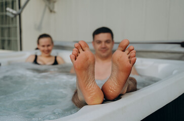 A man and a woman are relaxing in a warm jacuzzi, with the man exposing his wet heels in the...