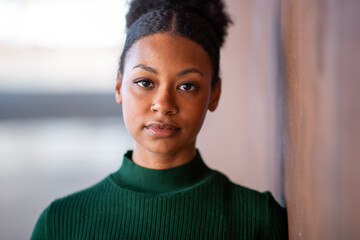 Close-up portrait of woman in green sweater leaning against wall