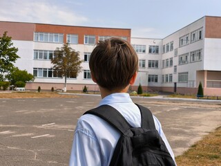 A boy looks at the school building. A thoughtful boy stands with his back to the school and looks...