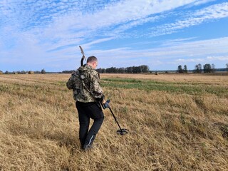 a man with a metal detector in an agricultural field. Man enjoying recreational archeology with...