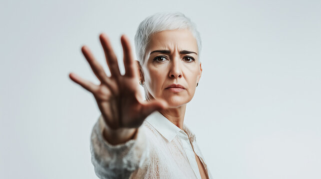 Confident mature woman with short white hair shows stop gesture saying no to violence, sexual harassment, femicide, discrimination and hate crime based on gender or skin color. 