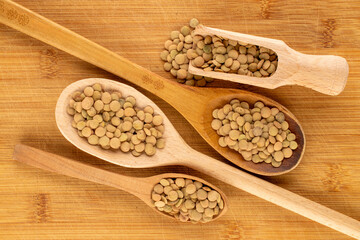 Lentil seeds with wooden spoons on a wooden table, close-up, top view.