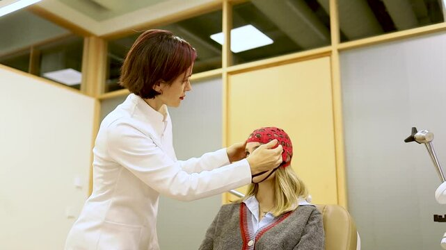 Video of a psychiatrist in a white coat places a measuring cap on a girl's head to use a transcranial magnetic stimulation device. TMS concept.