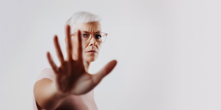 Mature woman with short white hair and glasses raising hand in stop gesture, serious expression, isolated on white background