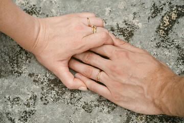 Two hands resting on stone with wedding bands &ndash; representing partnership